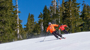 Skiers carving turns on a groomed slope with strong edging technique.