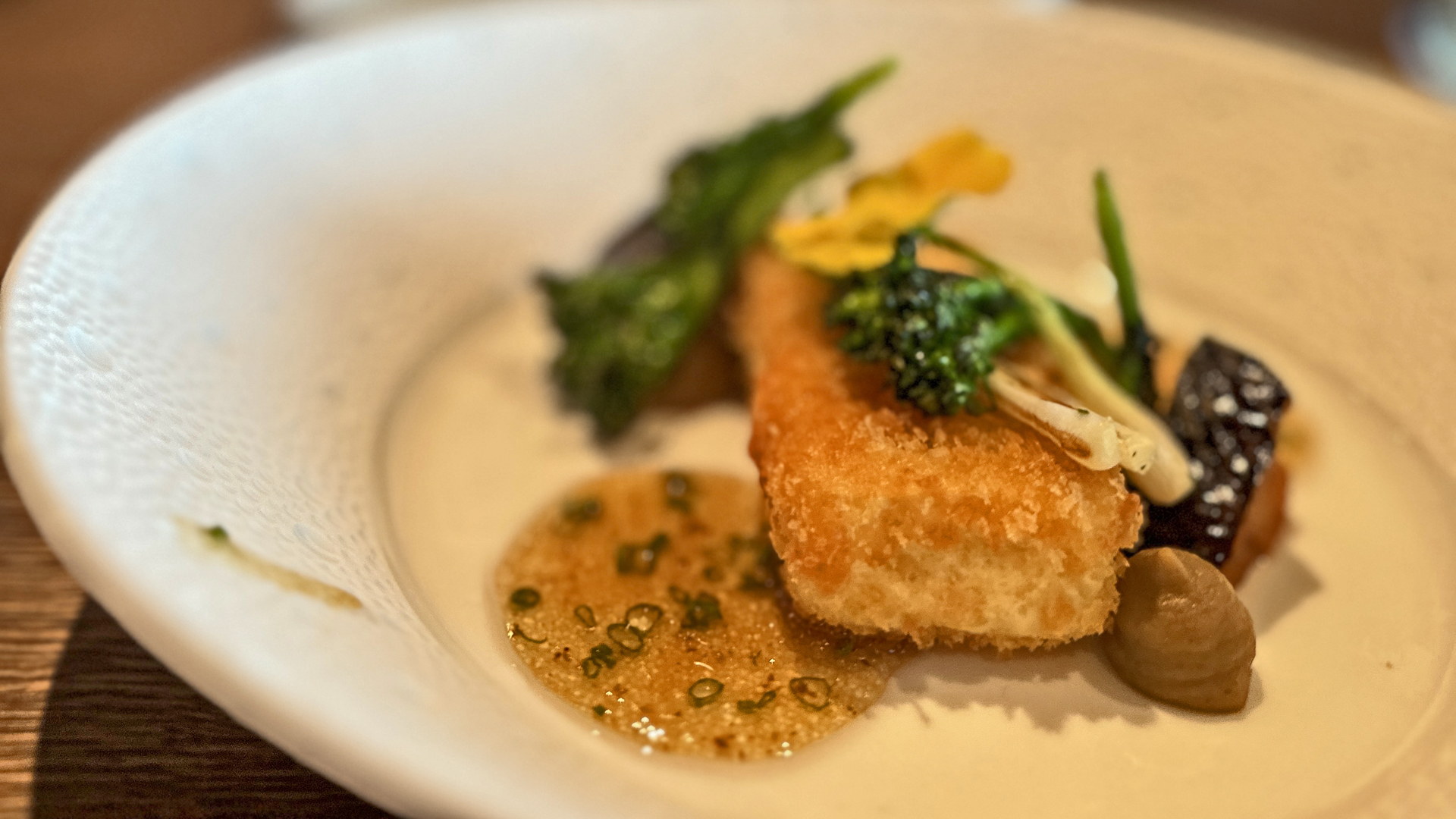 Close-up of a gourmet dish with crispy golden fish, vegetables, and sauce in Andermatt, Switzerland.